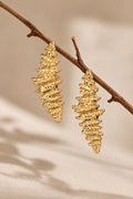 Textured gold earrings on beige backdrop with twig