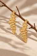 Textured gold earrings suspended from a twig