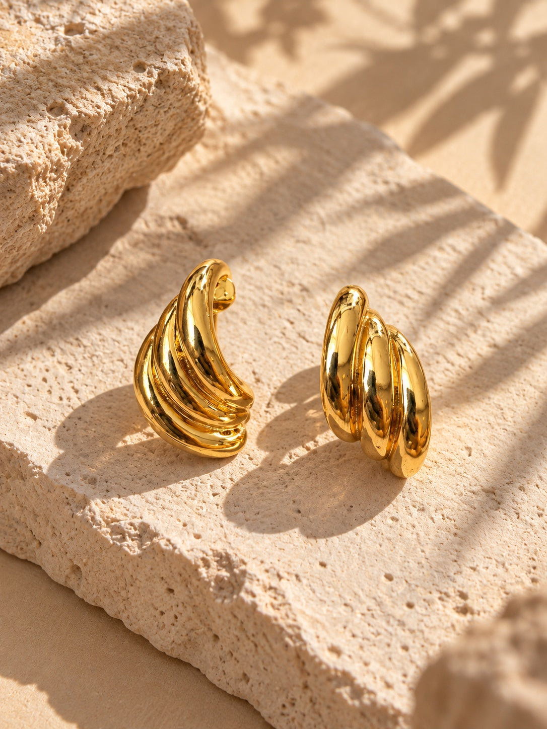 Close-up sculpted gold earrings on travertine