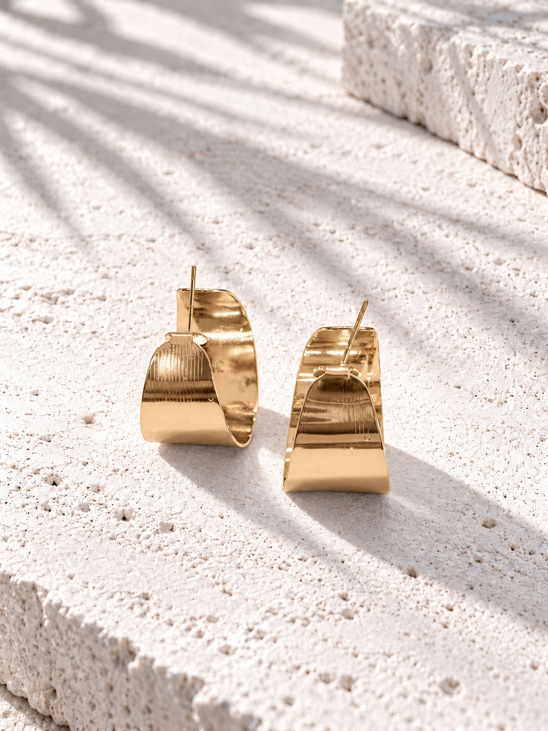 Niska gold-tone sculptural alloy hoop earrings on white travertine
