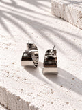 Niska silver-tone alloy statement hoop earrings on white travertine