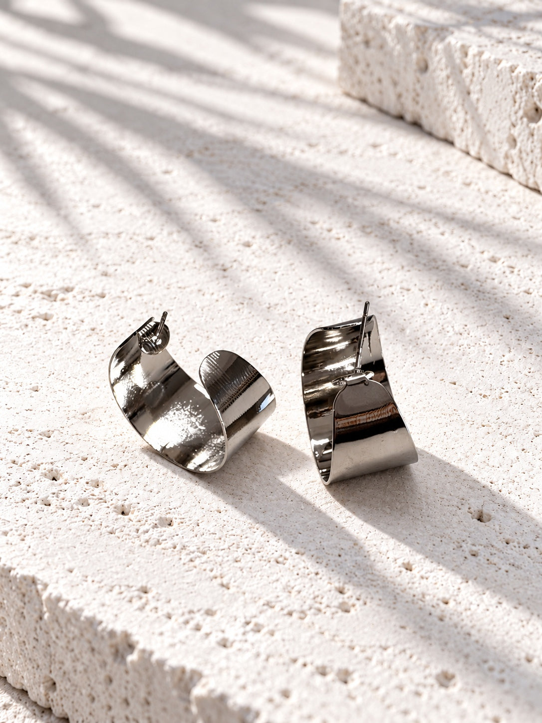 Niska silver-tone alloy statement hoop earrings on white travertine