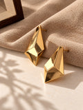 Gold geometric statement earrings on beige linen and stone backdrop, angle 2
