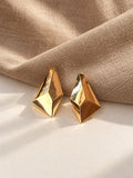 Gold geometric statement earrings on cream and beige textured backdrop