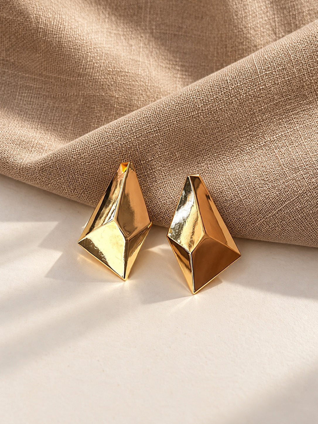 Gold geometric statement earrings on cream and beige textured backdrop