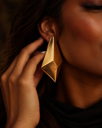 Model wearing Niska gold geometric statement earrings with softer, reduced lighting and muted shine