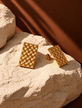 Gold woven rectangular earrings on textured stone, alternate angle