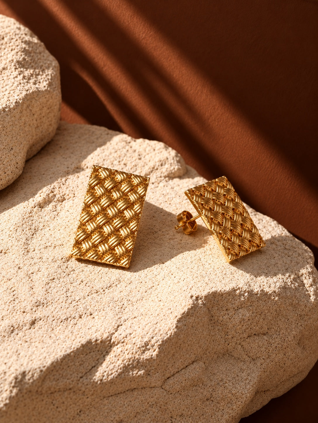 Gold woven rectangular earrings on textured stone, alternate angle