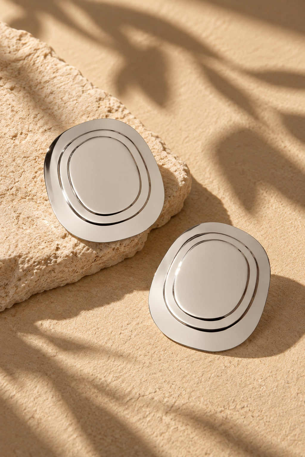 Silver oval statement earrings styled beside textured stone