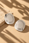 Silver concentric oval earrings in sunlight on beige backdrop