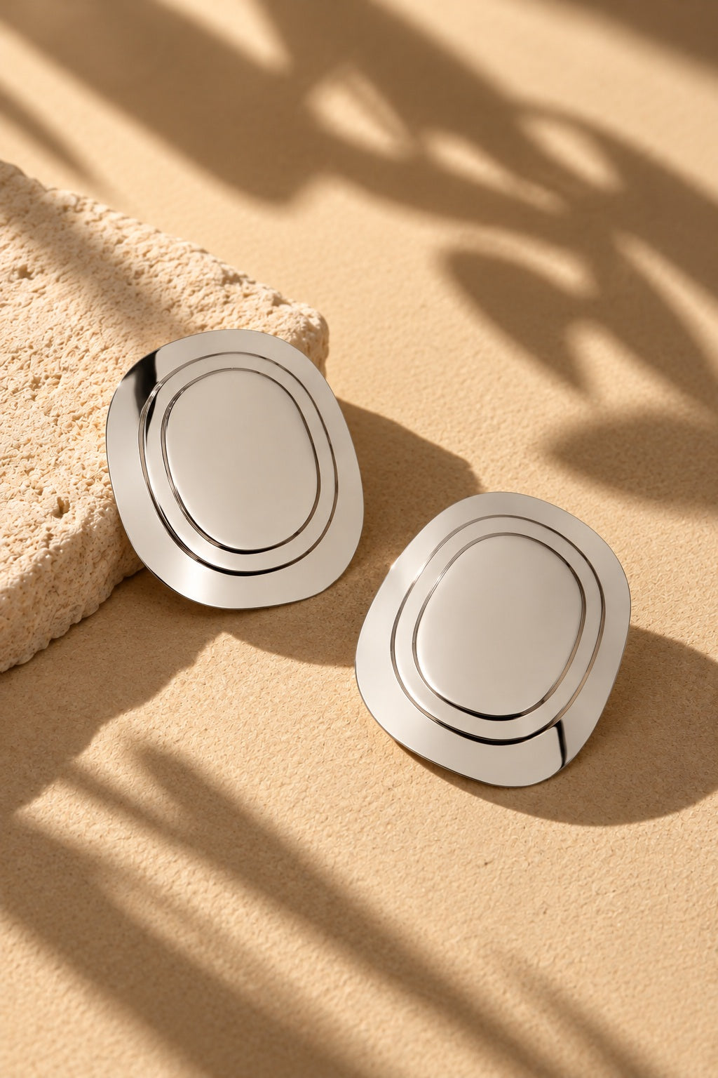 Silver concentric oval earrings in sunlight on beige backdrop