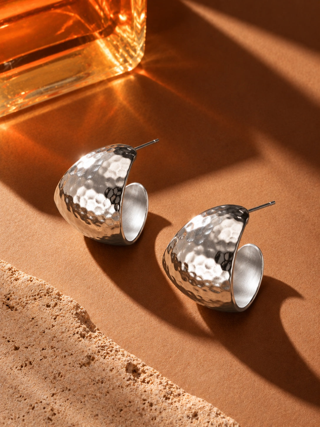 Silver hammered hoop earrings on warm amber stone backdrop