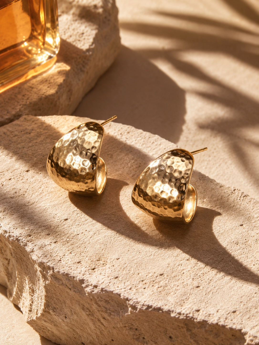 Hammered gold earrings on textured stone backdrop