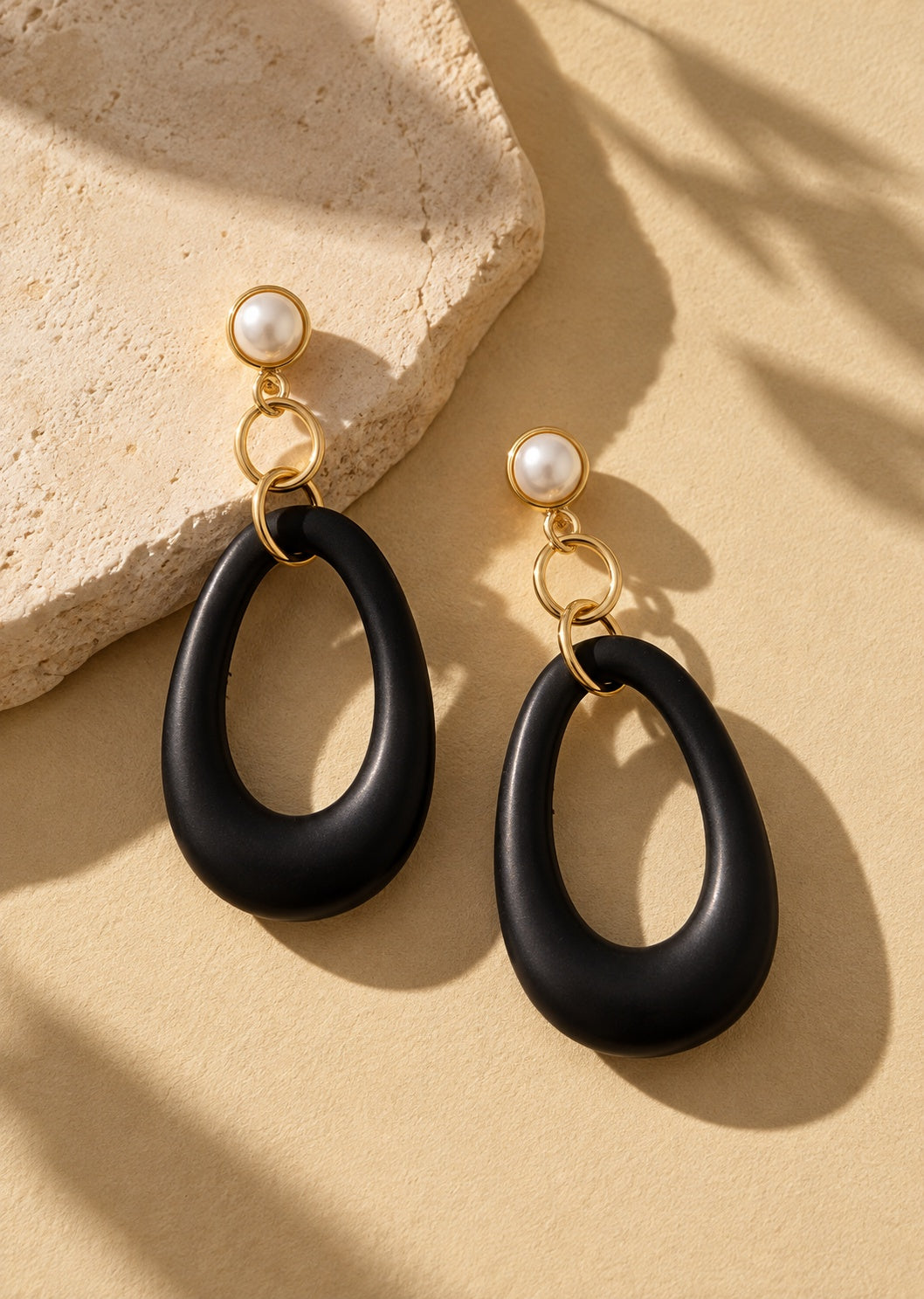 Black resin long earrings on beige stone backdrop