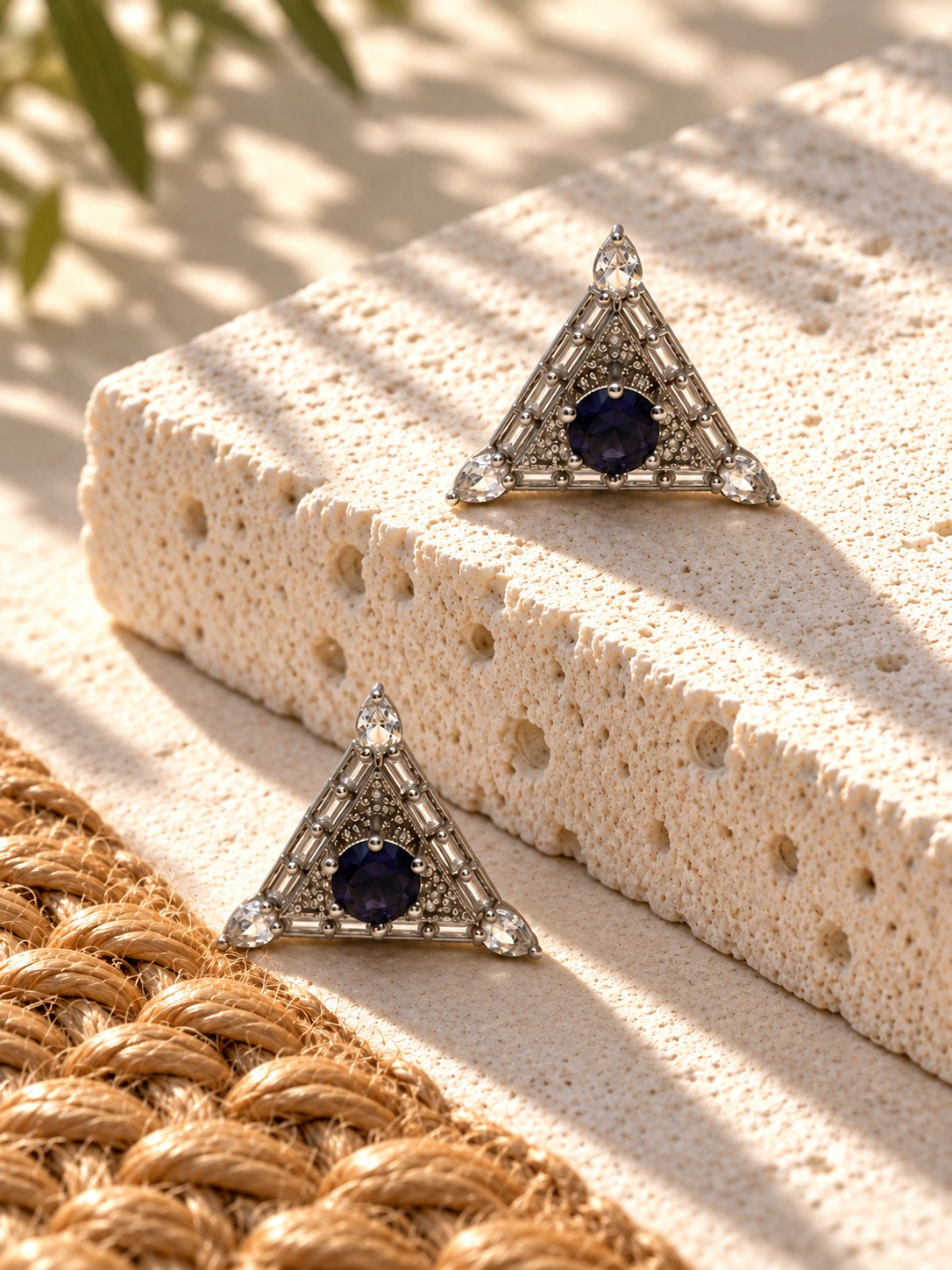 Niska triangular AD Stone Silver replica earrings, one on white travertine and one below beside jute