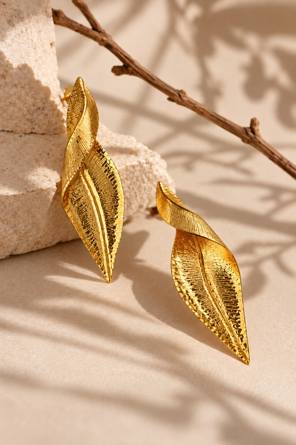 Gold leaf statement earrings arranged on a stone pedestal