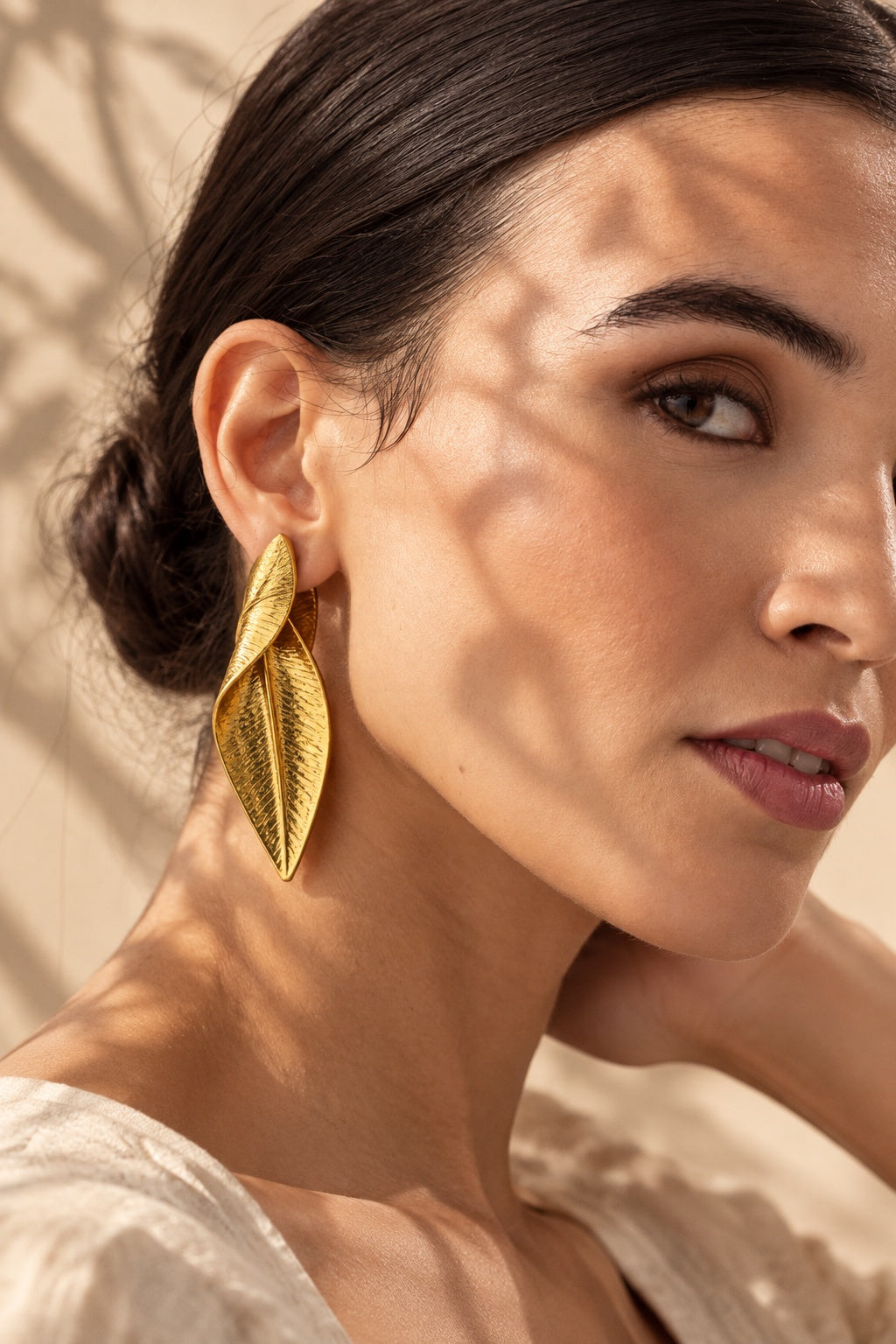 Close-up model wearing textured gold leaf statement earrings