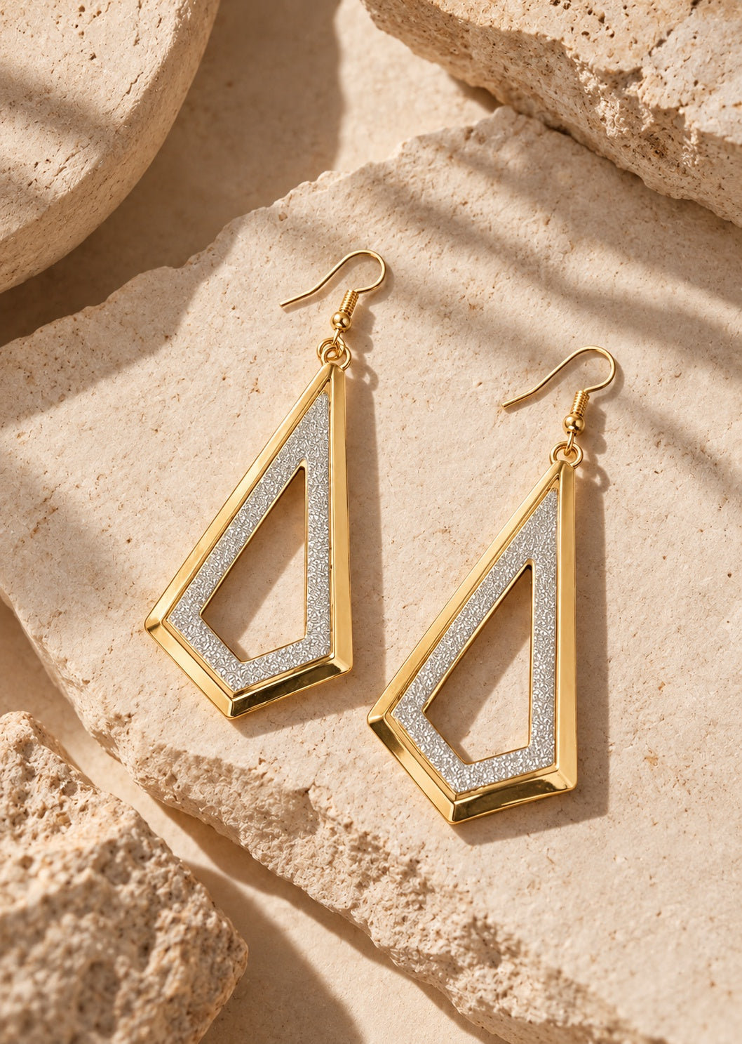 Flatlay of geometric gold and silver earrings on beige stone