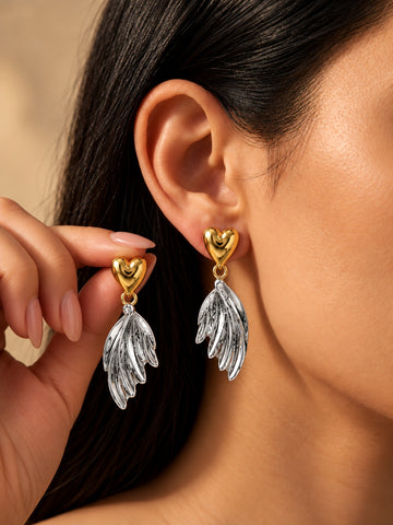 Niska dual-tone heart and wing drop earrings worn by model and held in hand