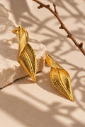 Textured gold leaf earrings on a cream stone surface