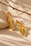 Textured gold leaf earrings beside a stone, editorial product angle